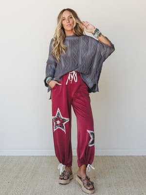 A relaxed, expressive outfit pairing an oversized grey cable-knit sweater with burgundy star-patch joggers — the kind of look that feels effortless but clearly thought about.