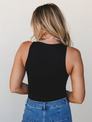 Shot from behind, this model wears a sleek black tank bodysuit tucked into medium-wash denim, finished with a colorful beaded necklace that gives the whole look a casual, personal touch.