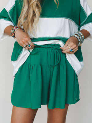 A color-block top and tiered mini skirt set in kelly green and ivory, styled with stacked beaded bracelets and silver rings — the kind of put-together-but-easy outfit that looks like you tried just the right amount.