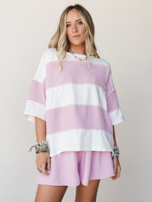 A relaxed two-piece matching set in wide-stripe orchid pink and ivory — the kind of outfit that looks just as good on a coffee run as it does on a beach boardwalk, styled with stacked beaded bracelets and a dainty layered necklace.