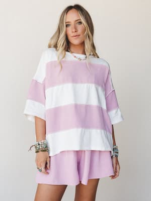 A relaxed two-piece matching set in wide-stripe orchid pink and ivory — the kind of outfit that looks just as good on a coffee run as it does on a beach boardwalk, styled with stacked beaded bracelets and a dainty layered necklace.
