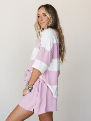 A relaxed matching set in orchid pink and ivory wide stripes — the oversized top ties at the waist over pull-on shorts, styled with stacked beaded bracelets for that effortless, off-duty feel.