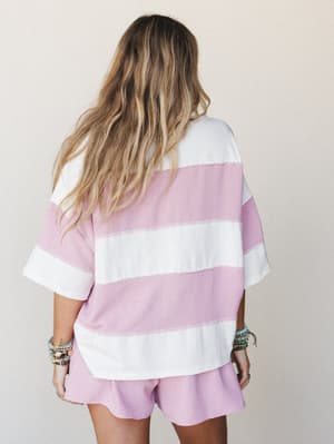 A back-view shot of a matching two-piece set — an oversized wide-stripe tee and relaxed shorts in orchid pink and ivory — styled with stacked boho bracelets for that effortlessly lived-in feel.