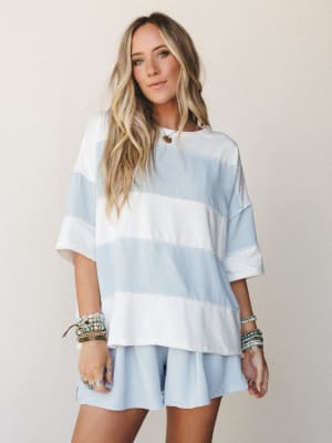 An oversized wide-stripe top and matching shorts set in soft sky blue and white, styled with layered beaded bracelets and a delicate necklace — the kind of effortless matching set that feels just as good as it looks.