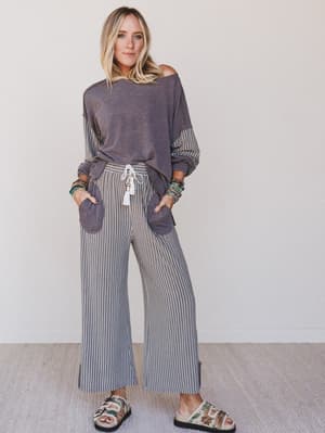 Woman wearing a gray off-shoulder top and striped pants with a white background