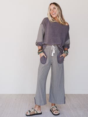 Woman wearing a purple off-shoulder top and striped pants against a white background