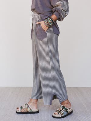 Person wearing a patterned shirt, striped pants, and floral sandals on a light background