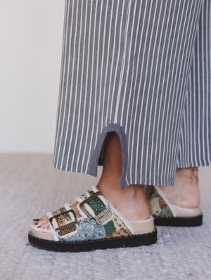 Colorful sandals worn with a striped dress on a neutral background