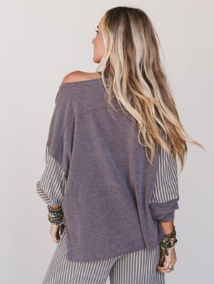 Person wearing a loose-fitting, off-shoulder top with long blonde hair on a plain background