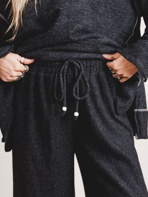 Person wearing a dark gray hoodie and matching pants with a plain background