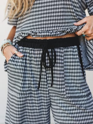A close-up torso shot of a matching gingham co-ord set — cropped top and wide-leg drawstring pants — styled with layered beaded bracelets and stacked rings for that effortless, off-duty boho feel.