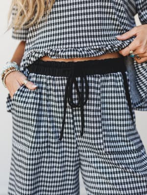 A close-up torso shot of a matching gingham co-ord set — cropped top and wide-leg drawstring pants — styled with layered beaded bracelets and stacked rings for that effortless, off-duty boho feel.