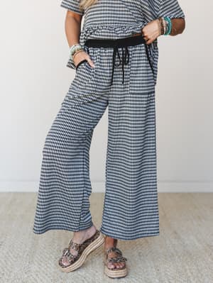 A gingham wide-leg pant with a black smocked waistband and drawstring tie, styled as a matching set with platform espadrille sandals and a stack of beaded bracelets — the kind of outfit that looks effortless but clearly had a little thought behind it