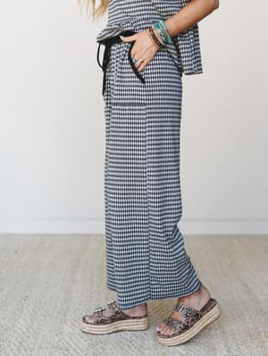 A side-profile shot of a gingham wide-leg pant set styled with leopard print platform sandals and a stack of beaded bracelets — casual and collected with just enough personality.