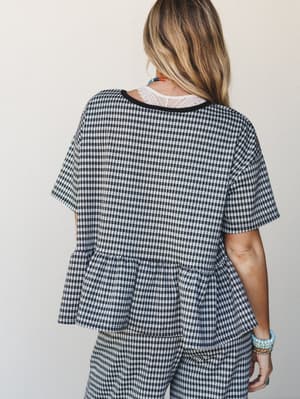 A back-facing shot of a gingham matching set — peplum top and wide-leg pants in black and white check — styled with layered beaded necklaces and turquoise bracelets for an effortless, expressive everyday look.
