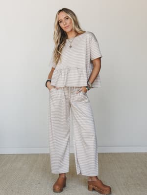 A matching gingham pant set in warm sand — peplum top and wide-leg drawstring pants styled with wood clogs and layered jewelry for an effortlessly put-together everyday look.