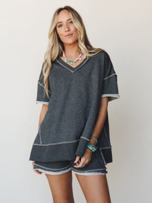 A relaxed charcoal matching set — oversized v-neck top and mini shorts with contrast exposed stitching — styled with colorful beaded jewelry for that effortless 'grabbed it off the chair and somehow looked great' energy.