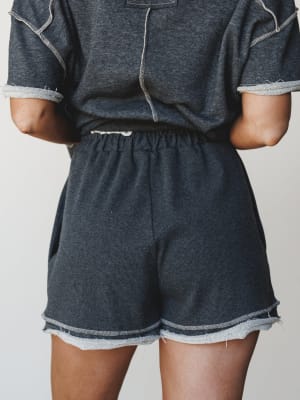 A close-up mid-shot of a matching charcoal sweat short set styled from the back — the raw-hem shorts and contrast-stitch tee feel effortlessly worn-in, like your favorite Saturday morning outfit that somehow always looks pulled together.