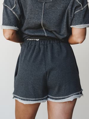 A close-up mid-shot of a matching charcoal sweat short set styled from the back — the raw-hem shorts and contrast-stitch tee feel effortlessly worn-in, like your favorite Saturday morning outfit that somehow always looks pulled together.