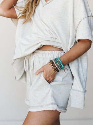 A relaxed short set in heathered light grey styled with a stack of beaded bracelets — the kind of outfit that looks this good whether you're making coffee or running errands.