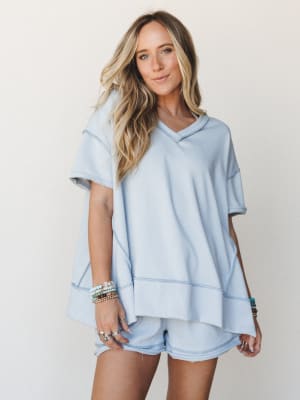 A soft sky blue matching short set — oversized hooded top and mini shorts — styled with stacked boho bracelets and silver rings for that effortless, I-just-threw-this-on energy.