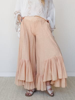 Dreamy wide-leg ruffle pants in a soft peach-coral gauze fabric, styled with a white embroidered top and sandals — the kind of outfit that makes a farmers market feel like a whole moment.