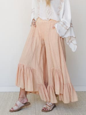 A dreamy wide-leg pant in soft peach gauze with voluminous ruffle hems, styled with an embroidered white top and buckle sandals — the kind of outfit that makes a Tuesday feel intentional.