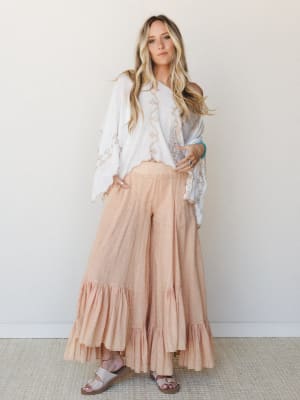 A flowy, wide-leg ruffle pant in soft peachy coral paired with an embroidered white poncho top — the kind of outfit that looks equally at home at a coastal market or a backyard gathering.