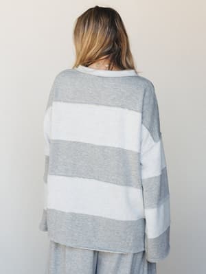 A model shot from behind showing an oversized wide-stripe sweatshirt in heather gray and white, paired with matching wide-leg heather gray pants — the kind of set that makes staying in feel intentional.