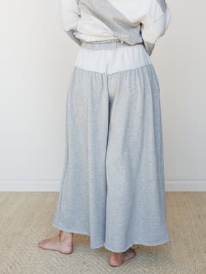 A relaxed, wide-leg heather gray pant with a color-block waistband and flowy, almost skirt-like silhouette — shot from the back on a barefoot model in a soft, neutral interior.