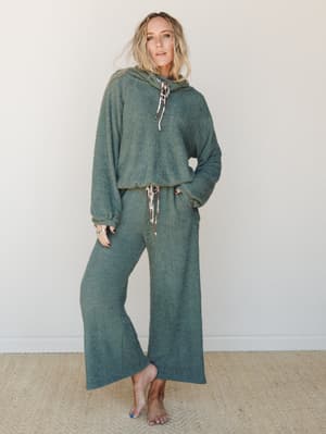 A matching boucle hoodie and wide-leg pant set in a muted sage green, styled barefoot against a soft neutral wall — the kind of outfit that makes staying home feel intentional.