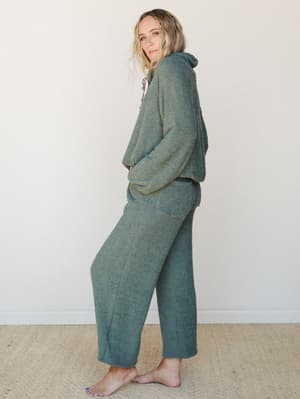A matching boucle lounge set in a muted sage-meets-teal basil green — the kind of set that makes staying home feel intentional, worn here with effortless side-glance energy against a soft studio wall.