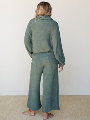 Shot from the back, a model wears a matching boucle lounge set in a muted sage-teal — the kind of outfit that makes staying home feel like a whole personality.