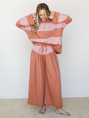 A relaxed two-piece set in warm camel and dusty pink, styled on a smiling model with hands in her hair — the kind of outfit that makes a Saturday morning feel intentional.