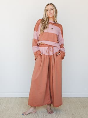 A relaxed two-piece set in warm camel and dusty mauve colorblocking — wide-leg pants with a drawstring waist paired with a long-sleeve cropped top, styled barefoot against a clean white wall for an effortlessly lived-in feel.