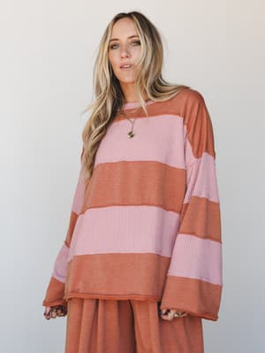 An oversized striped thermal top in dusty pink and camel rust is styled with matching wide-leg pants, giving off that effortlessly cozy, 'stayed in but made it look good' energy.