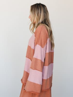 A side-profile shot of a model in an oversized color-block thermal top with wide bold stripes in terracotta and dusty pink — the kind of top that makes a Saturday morning feel intentional.