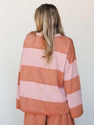 Shot from behind, a model wears an oversized striped thermal top in soft pink and terracotta, paired with matching wide-leg pants — the kind of set that makes a Saturday feel intentional.