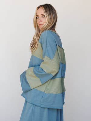 Shot from behind with a glance back over the shoulder, this mixed-media patchwork pullover pairs a dusty teal sweatshirt fabric with sage green waffle knit panels — effortlessly relaxed and a little unexpected, styled with a matching teal wide-leg pa