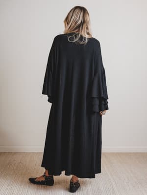 Woman wearing a black duster with ruffled sleeves in a minimal indoor setting