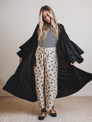 Woman wearing a black duster, striped shirt, and floral pants on a plain background