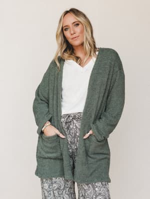 A cozy, oversized boucle cardigan in deep basil green layered over a white v-neck tee and grey paisley wide-leg pants — the kind of effortless outfit that looks pulled-together without trying.