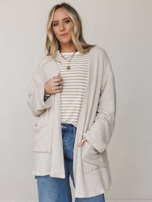 An oversized boucle cardigan in warm seashell layered over a striped tee and wide-leg jeans — the kind of effortless, stay-in-it-all-day outfit that somehow still looks pulled together.