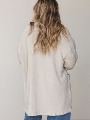 Shot from behind, a model in a oversized oatmeal boucle cardigan paired with blue denim — the kind of cozy layer you reach for without thinking and never want to take off.