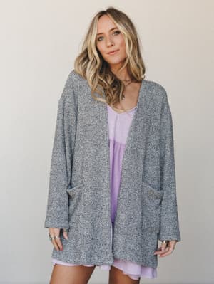 A relaxed, oversized marled knit cardigan in heathered grey layered over a soft lavender mini dress — the kind of outfit that looks like you tried just enough and felt great doing it.