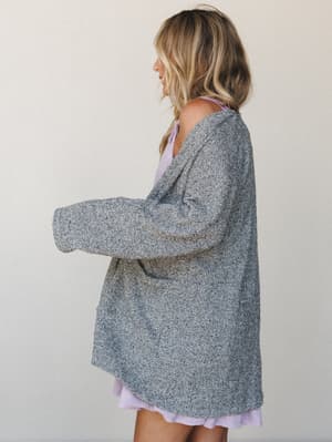 A heathered charcoal boucle cardigan layered over a soft lavender mini dress — the kind of effortless outfit that looks like it came together in two minutes but feels completely intentional.