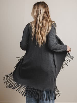 Person wearing a dark gray cardigan with fringe details on a plain background