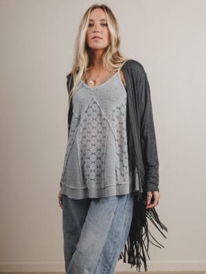 Woman wearing a floral top, gray cardigan with fringe, and jeans against a plain background