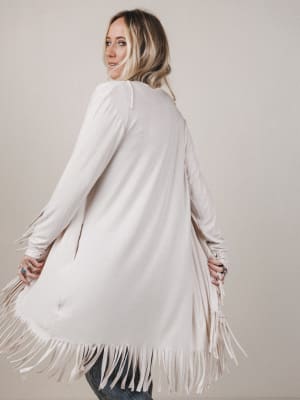 Woman wearing a white fringe cardigan against a plain background