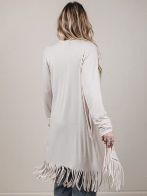 Person wearing a long beige cardigan with fringe details on a plain background